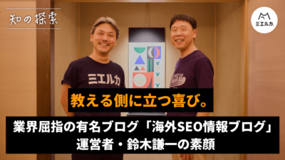 タイトル「教える側に立つ喜び。業界屈指の有名ブログ「海外SEO情報ブログ」運営者・鈴木謙一の素顔」 掛け軸を前に二人で立っている。 左側に本田、右側に鈴木。